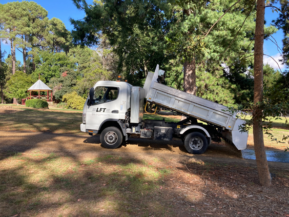 White truck pours seal for footpath in historic park with rotunda in background