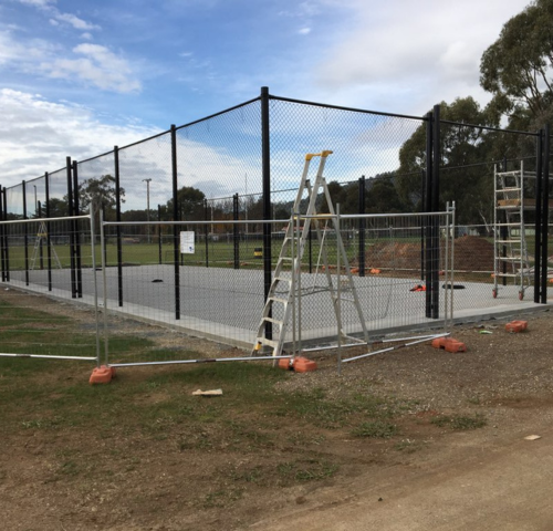 Construction site of new cricket nets showing newly poured concrete slab and chain mesh fencing with security fencing and ladders in foreground