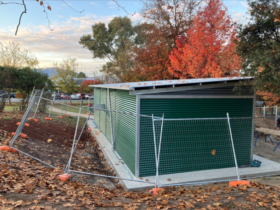 Construction of new toilet facility, surrounded by security fencing amidst orange and red autumn toned trees