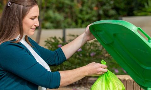 Woman dropping a green bag from a kitchen caddy in to the green organics bin